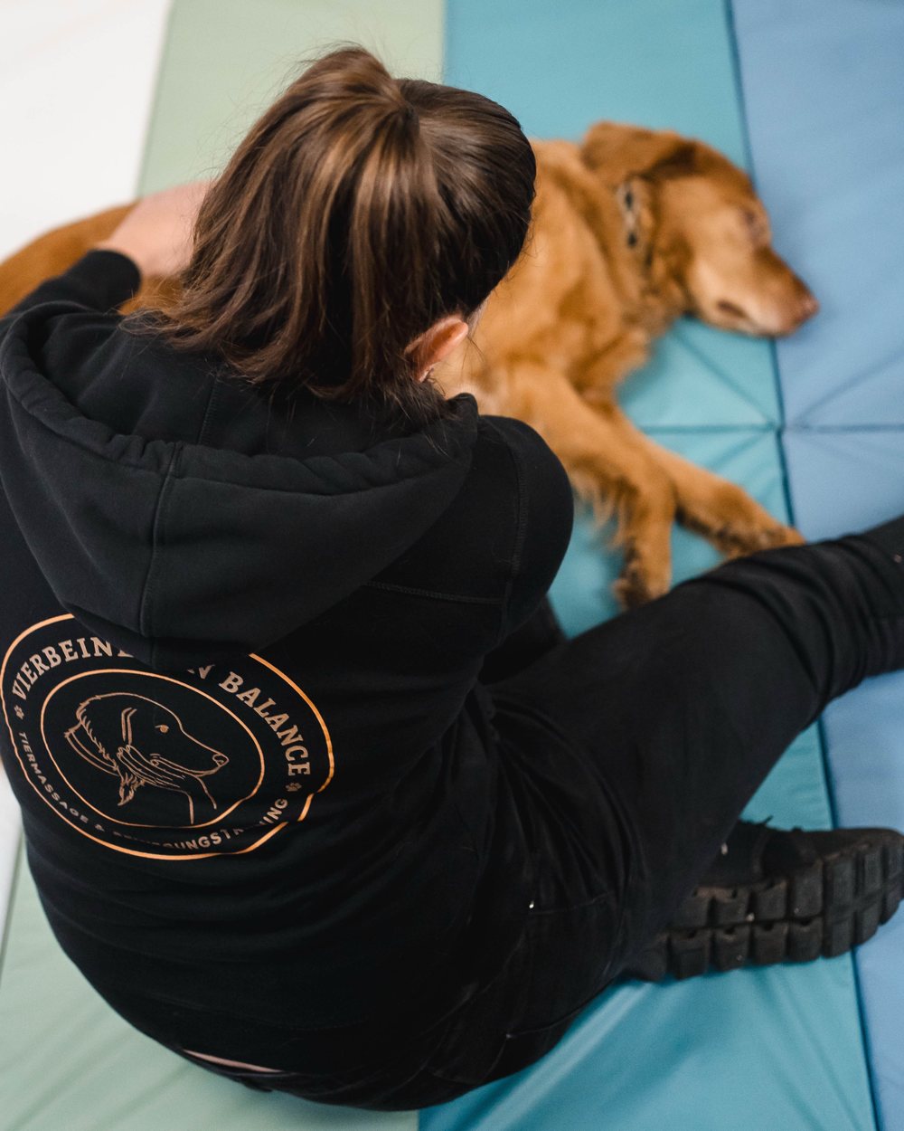 Anna sitzt auf einer Matte neben einem entspannt liegenden Hund